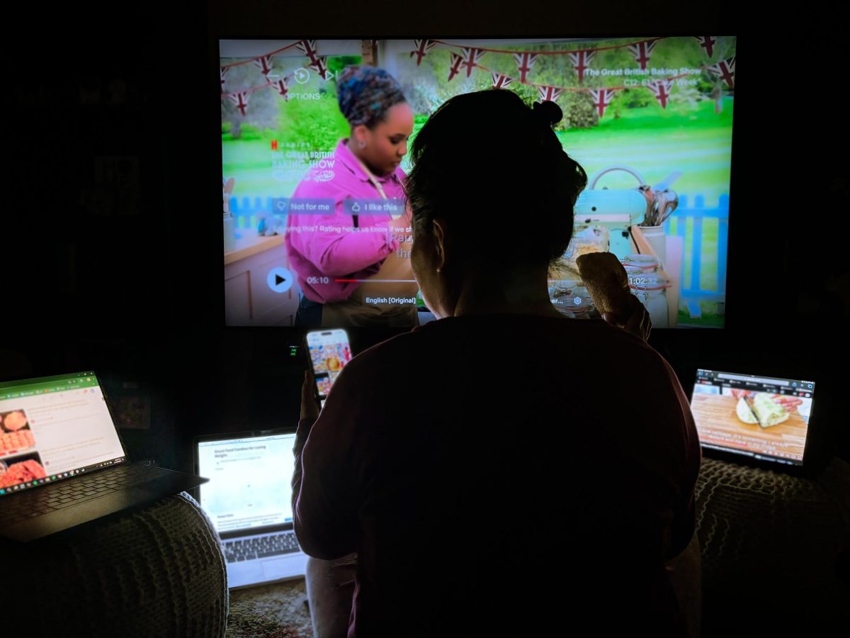 A silhouette of a woman eats a piece of bread, enraptured by the surrounding screens.