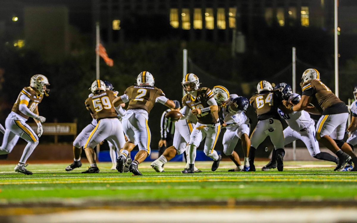 Aaron Knapp (’25) hands the ball off to Kingston Keananiana (’25) while the offensive line blocks.