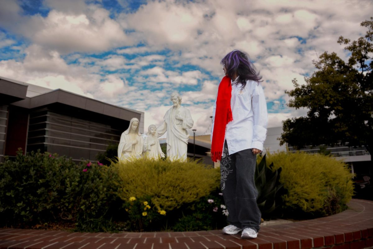 Liturgy student stares thoughtfully at the statue of the Holy Family, carrying a scarf the color of the Holy Spirit.