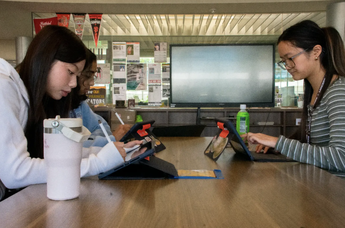 Nanditha Venkatasubramanian ('27), Bethany Ma ('27), and Valerie Lee ('27) work on their iPads in the library.